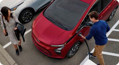 Man charging his red EV at a charging station while a woman looks on